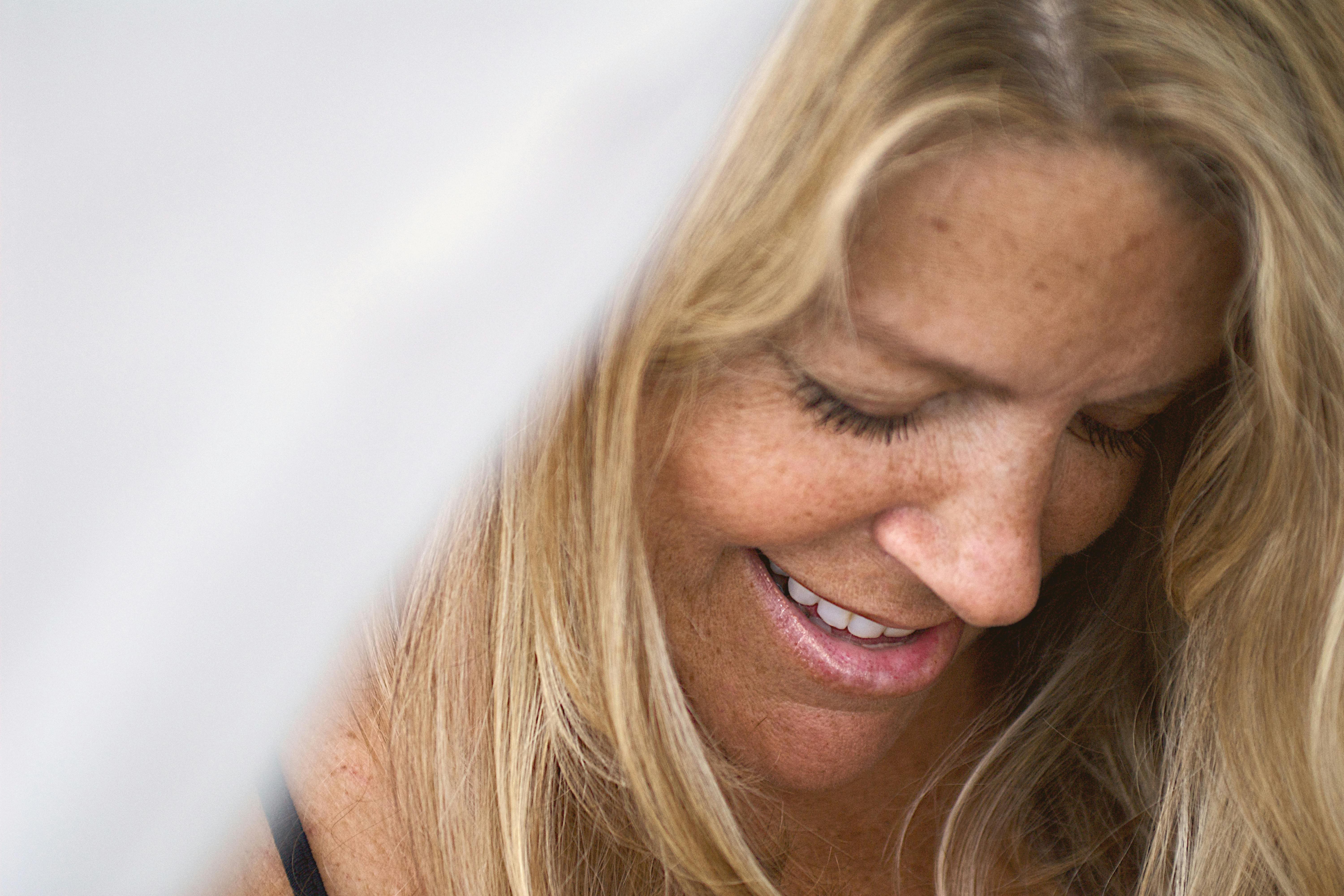 A woman smiling softly, looking down, with warm natural light